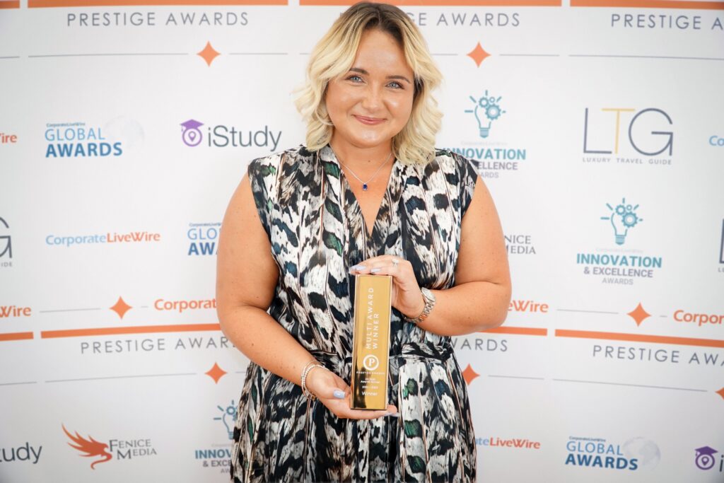 A lady is stood holding an award in front of her, facing the camera and smiling,