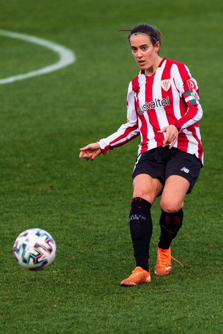 A woman is running down a football pitch with a ball at her feet