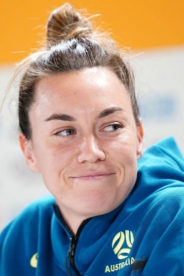 A close up image of a woman's face with her long hair tied up away from her face. She is looking at someone to the side of her off camera and smiling.