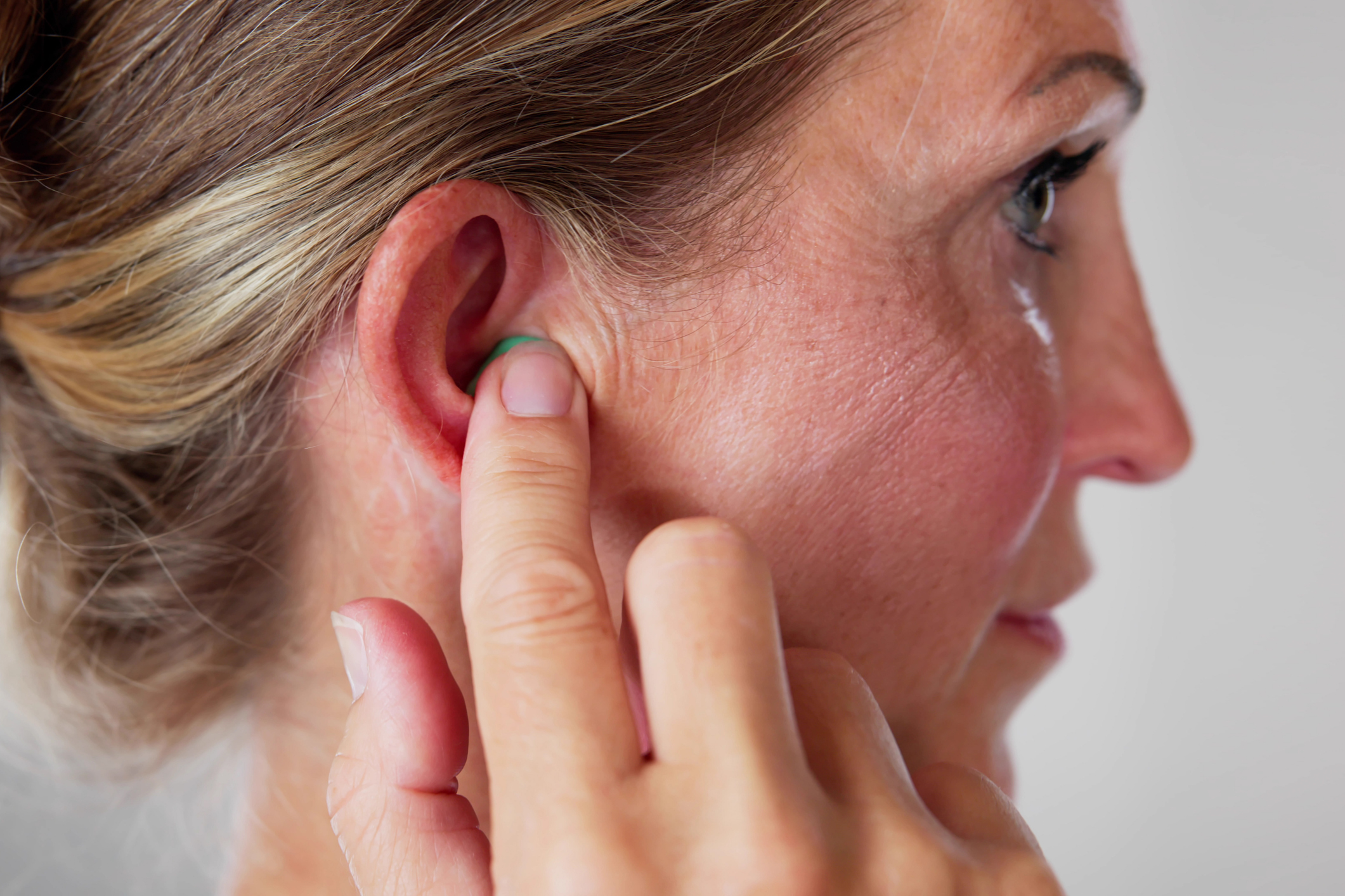 A photo of the side of a woman's face, she is holding a small ear plug in her ear with her index finger